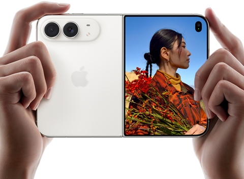 جهاز iPhone Duo، لون أبيض النجوم، يدان تحملان الجهاز في الوضع الأفقي، مفتوح، اللوحة اليسرى تعرض الكاميرا المزدوجة 48MP Fusion الخلفية، اللوحة اليمنى تعرض شخصاً تُلتقط صورته على الشاشة الخارجية، يمكن لهذا الشخص رؤية وجهه لأن الصورة تُلتقط باستخدام ميزة Duo Preview