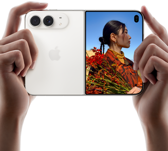 جهاز iPhone Duo، لون أبيض النجوم، يدان تحملان الجهاز في الوضع الأفقي، مفتوح، اللوحة اليسرى تعرض نظام كاميرا مزدوجة 48MP Fusion، اللوحة اليمنى تعرض شخصاً تُلتقط صورته على الشاشة الخارجية، يمكن لهذا الشخص رؤية وجهه لأن الصورة تُلتقط باستخدام ميزة Duo Preview